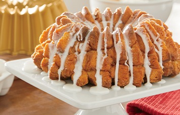 Bundt cake with white icing drizzled over it, displayed on a white square cake stand